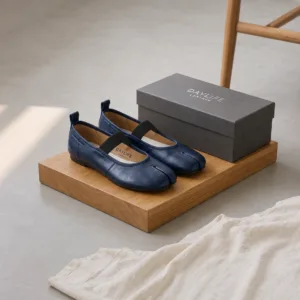 A pair of premium DayLife Leather navy blue tabi-toe Mary Jane flat shoes with black elastic straps, displayed on a wooden block next to a branded grey shoe box at DayLifeLeather.com.
