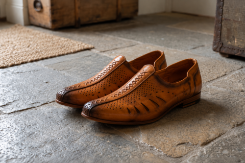 Side view of a pair of men's tan genuine leather mojari style loafers, featuring laser-cut breathable design and a burnished dual-tone finish.
