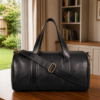 Premium black genuine leather duffle bag with adjustable shoulder strap, displayed in a modern lifestyle setting with natural lighting.
