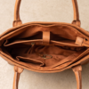 Open profile view of a DayLife Leather women's shoulder bag in a peach-pink hue, resting on a dark wood table with blurred background books.