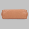 Base profile view of a DayLife Leather women's shoulder bag in a peach-pink hue, resting on a dark wood table with blurred background books.