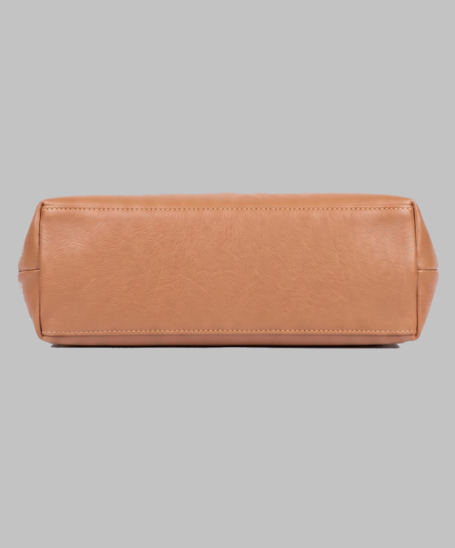 Base profile view of a DayLife Leather women's shoulder bag in a peach-pink hue, resting on a dark wood table with blurred background books.