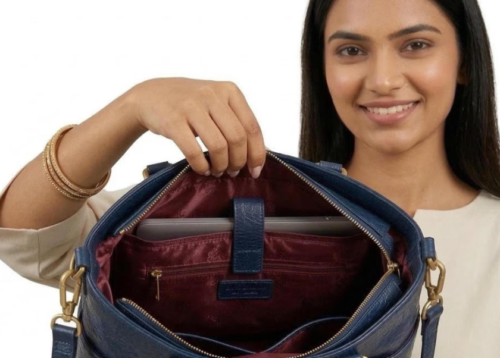 Front view of a dark blue croc-embossed leather tote bag by DayLife Leather, featuring gold hardware, an adjustable strap, and a brown leather logo tag, resting on a wooden table.