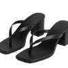 A pair of DayLife Leather black square-toe heeled sandals with thong-style straps, displayed on a rustic stone tiled floor surrounded by terracotta planters at DayLifeLeather.com.