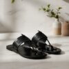Handcrafted black leather toe ring sandals with braided strap detail on a marble surface