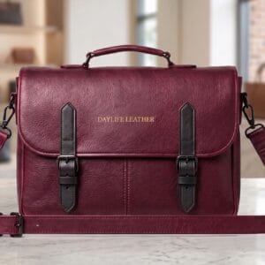 daylife-leather-burgundy-messenger-bag Handcrafted burgundy leather messenger bag with black buckle straps and top handle by DayLife Leather, displayed on a white marble tabletop.