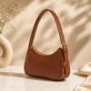 Perspective view of DayLife Leather tan brown pebbled leather shoulder bag with adjustable strap, gold buckle, and zipper closure.