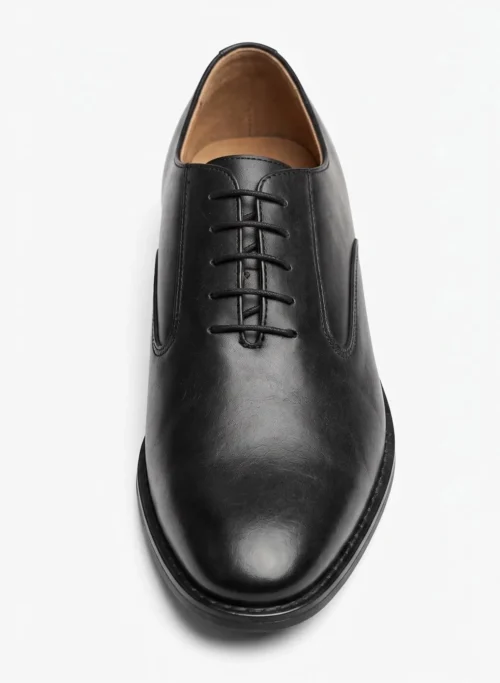 Three-quarter front angle view of a pair of polished black leather Oxford shoes isolated on a white background.