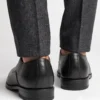 Back view of men's black leather Oxford shoes worn with grey trousers, showing the heel construction and stitching.
