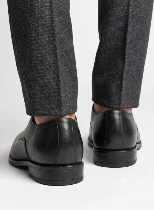 Back view of men's black leather Oxford shoes worn with grey trousers, showing the heel construction and stitching.