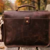 DayLife Leather vintage brown full-grain leather messenger bag resting on a wooden bench in a park.