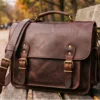 DayLife Leather vintage brown full-grain leather messenger bag resting on a wooden bench in a park.