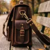 DayLife Leather vintage brown full-grain leather messenger bag resting on a wooden bench in a park.