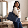 Open top view of navy blue leather bag showing spacious interior lining, zip compartment, and pockets Navy blue handcrafted leather tote bag with sturdy shoulder straps and side pockets on a display stand.