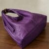 Deep purple genuine leather hobo bag with gold buckle strap on wooden surface