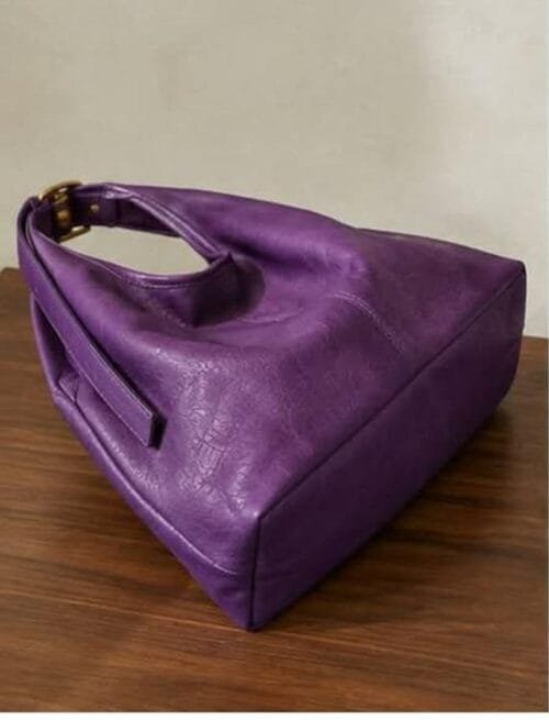 Deep purple genuine leather hobo bag with gold buckle strap on wooden surface