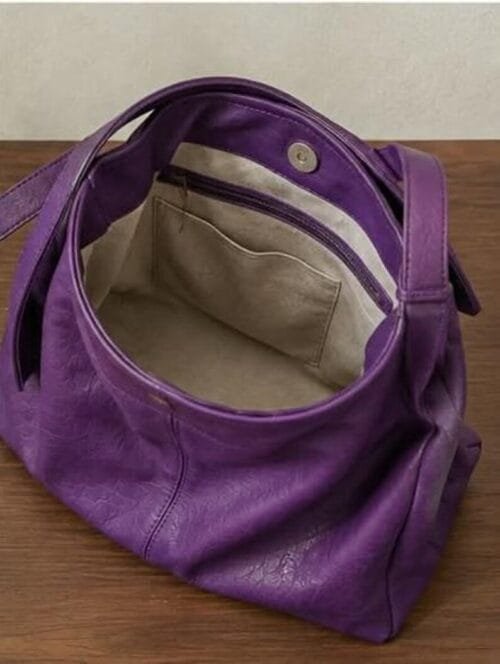 Deep purple genuine leather hobo bag with gold buckle strap on wooden surface