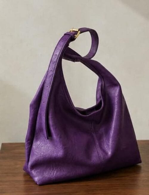 Deep purple genuine leather hobo bag with gold buckle strap on wooden surface