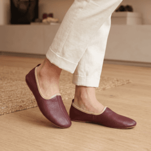 Men's maroon leather juti slip-on shoes with beige piping and suede-lined interior, side view