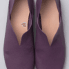 A product photography composite image showing a pair of handcrafted deep purple, pebbled leather flat shoes arranged in three views on a light gray background. The left panel shows the top-down (upper) view, the center panel shows the side profile, and the right panel shows the rear (back) view.