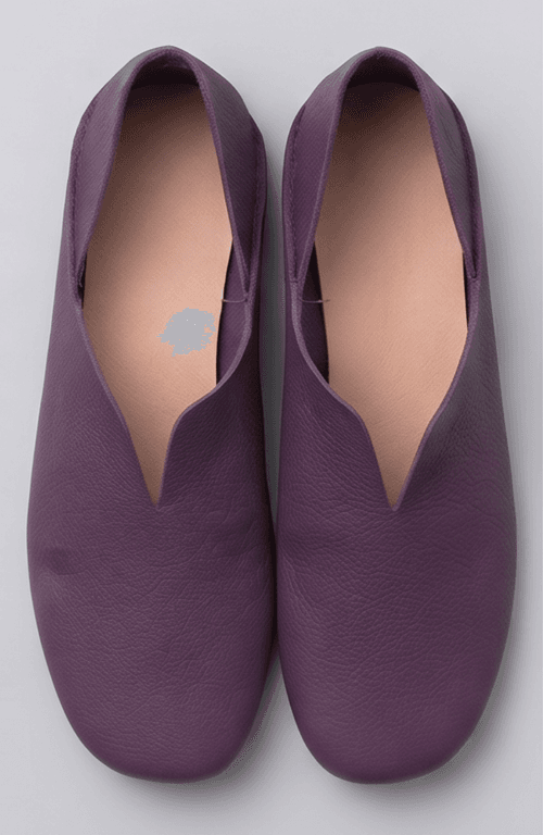 A product photography composite image showing a pair of handcrafted deep purple, pebbled leather flat shoes arranged in three views on a light gray background. The left panel shows the top-down (upper) view, the center panel shows the side profile, and the right panel shows the rear (back) view.