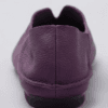 A product photography composite image showing a pair of handcrafted deep purple, pebbled leather flat shoes arranged in three views on a light gray background. The left panel shows the top-down (upper) view, the center panel shows the side profile, and the right panel shows the rear (back) view.