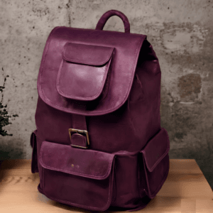 n aged purple leather backpack with multiple pockets on a wooden surface in front of a concrete wall.