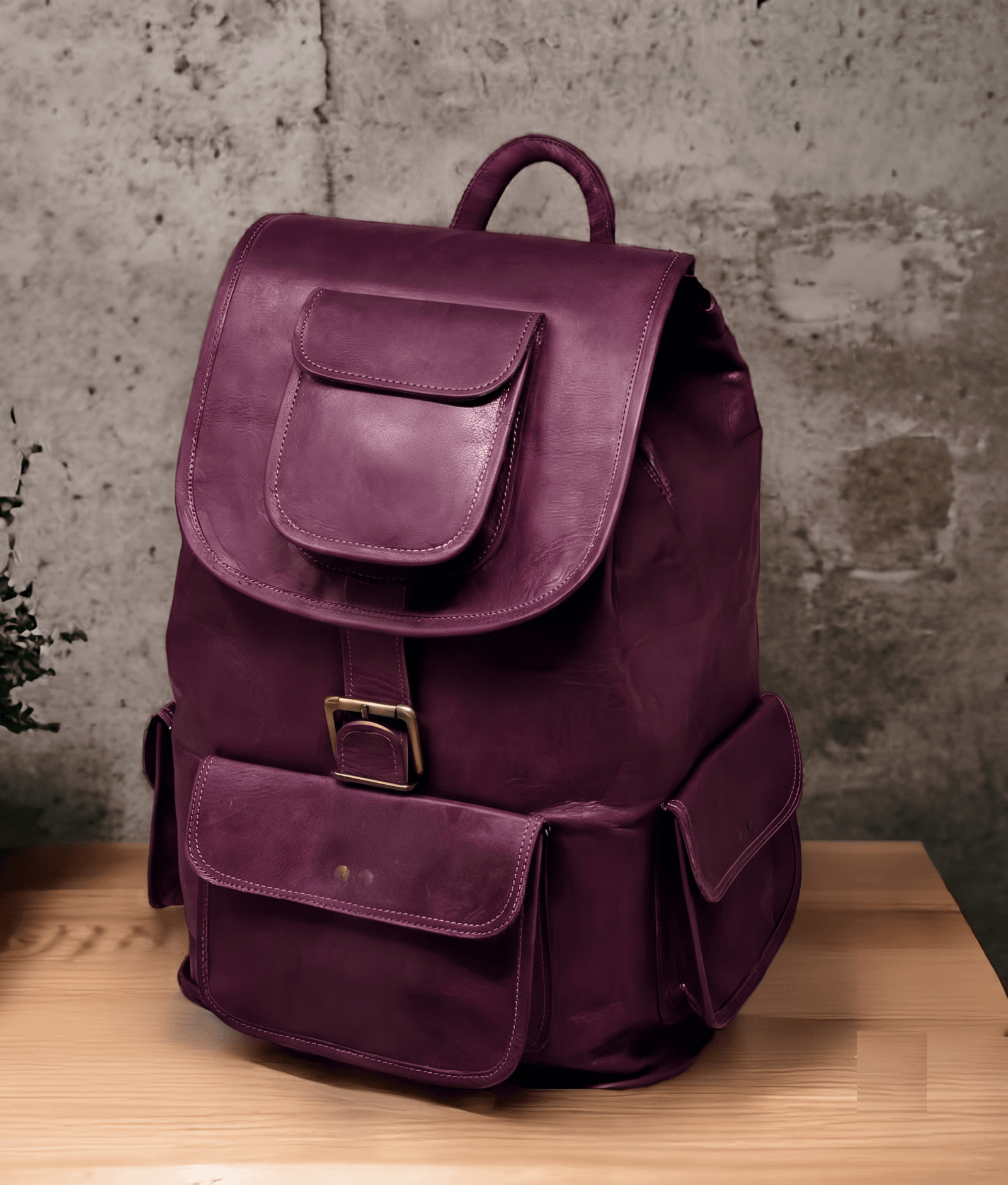 n aged purple leather backpack with multiple pockets on a wooden surface in front of a concrete wall.