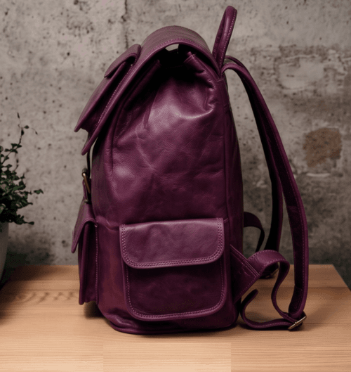 An aged purple leather backpack with multiple pockets on a wooden surface in front of a concrete wall.