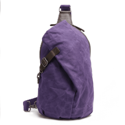 Male model wearing a vintage purple waxed canvas crossbody sling backpack by Daylife Leather on an urban cobblestone street, featuring product close-up and open interior view.