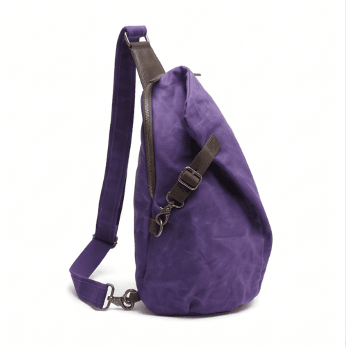 Male model wearing a vintage purple waxed canvas crossbody sling backpack by Daylife Leather on an urban cobblestone street, featuring product close-up and open interior view.