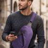 Male model wearing a vintage purple waxed canvas crossbody sling backpack by Daylife Leather on an urban cobblestone street, featuring product close-up and open interior view.